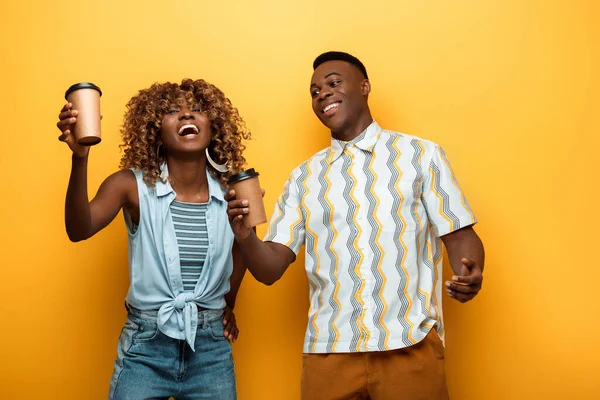 Happy african american couple with paper cups on yellow colorful background — Stock Photo