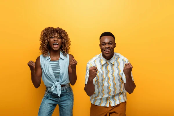 Feliz africano americano pareja mostrando sí gesto en amarillo colorido fondo - foto de stock