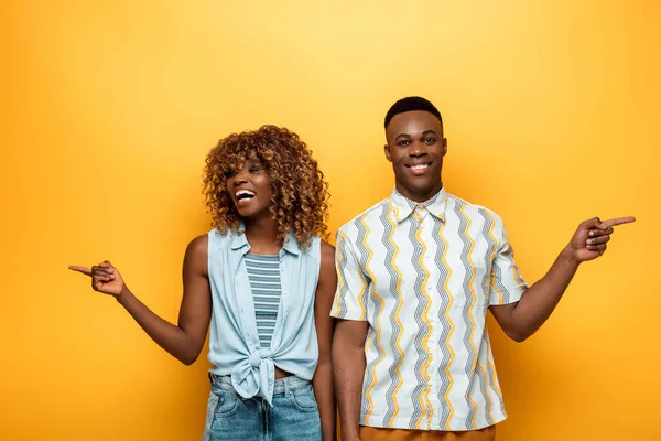 Щаслива афро-американська пара вказує пальцями на жовтий барвистий фон — стокове фото