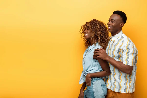 Vue latérale de heureux couple afro-américain sur fond jaune coloré — Photo de stock