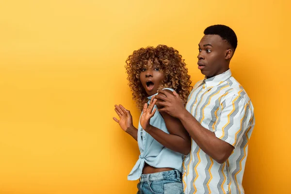 Vue latérale du couple afro-américain effrayé sur fond jaune coloré — Photo de stock