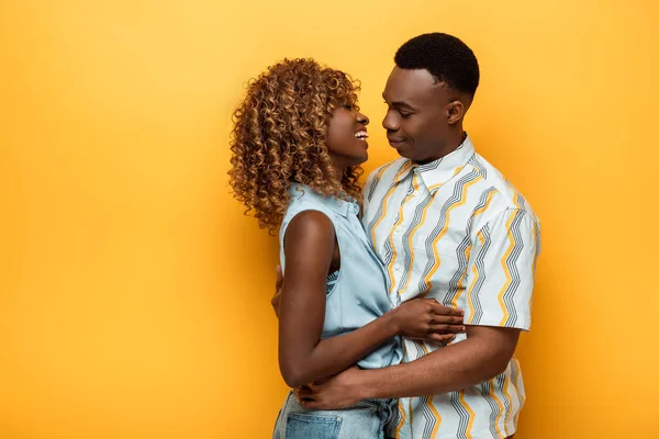 Vue latérale de heureux couple afro-américain étreignant sur fond jaune coloré — Photo de stock