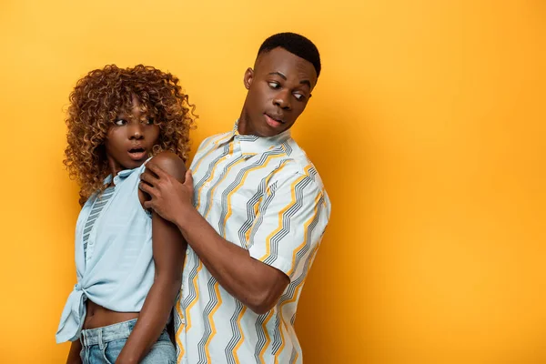 Vista lateral do casal afro-americano assustado olhando para longe no fundo colorido amarelo — Fotografia de Stock