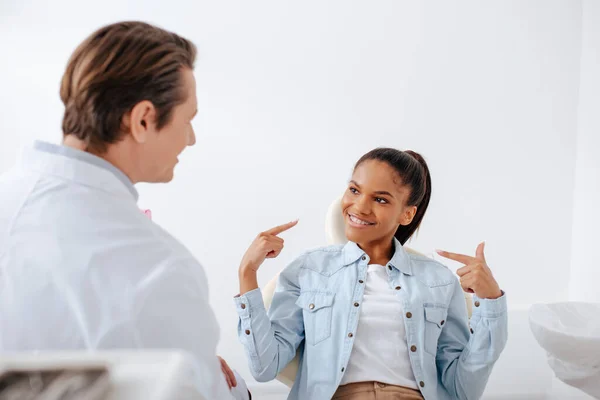 Enfoque selectivo de la mujer afroamericana feliz señalando con los dedos a los aparatos ortodoncistas cerca en la clínica - foto de stock