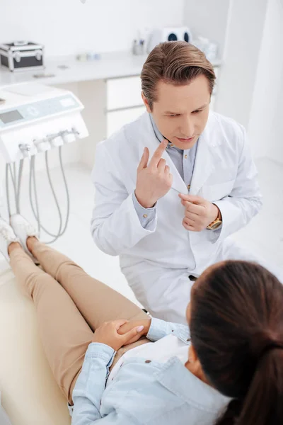 Vista aérea del dentista apuntando con el dedo a la boca y mirando al paciente afroamericano - foto de stock