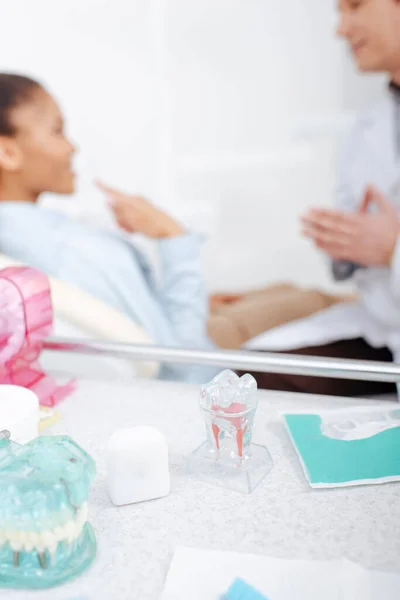 Selective focus of teeth models on surface near dentist and african american patient — Stock Photo