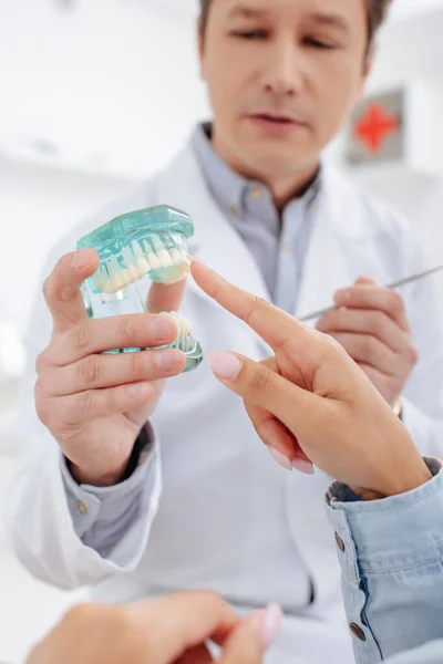 Selective focus of dentist in white coat near patient pointing with finger at teeth model — Stock Photo