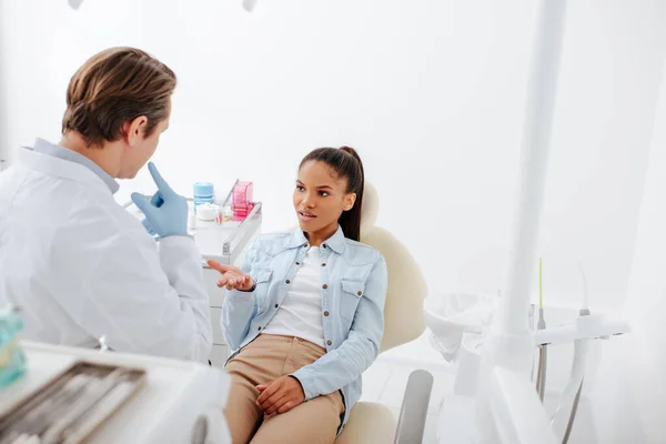 Enfoque selectivo del paciente afroamericano mirando al dentista señalando con el dedo en la cara - foto de stock
