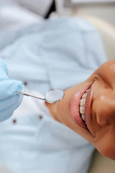 Vista superior de ortodoncista en guante de látex sosteniendo espejo dental cerca de paciente afroamericano feliz en frenos - foto de stock