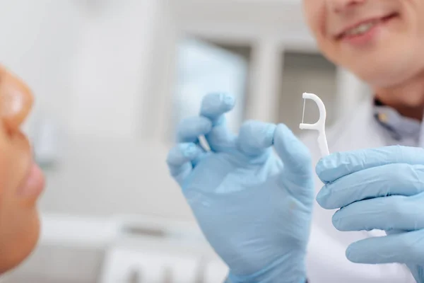 Vista recortada de dentista en guantes de látex sosteniendo palo de seda dental cerca de mujer afroamericana - foto de stock