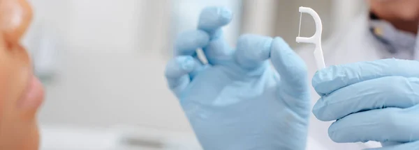 Panoramic shot of dentist in latex gloves holding floss stick near african american woman — Stock Photo