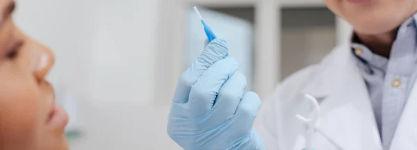 Tiro panorâmico de dentista segurando fio dental vara e escova de limpeza inter-dental perto de mulher afro-americana — Fotografia de Stock