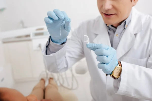 Обрезанный вид стоматолога, держащего зубную нить рядом с африканской американкой — стоковое фото