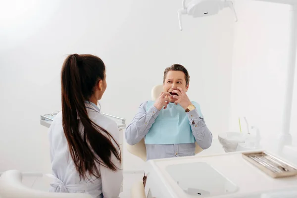 Rückansicht eines afrikanisch-amerikanischen Zahnarztes, der in der Nähe eines verängstigten Patienten sitzt und das Gesicht berührt — Stockfoto