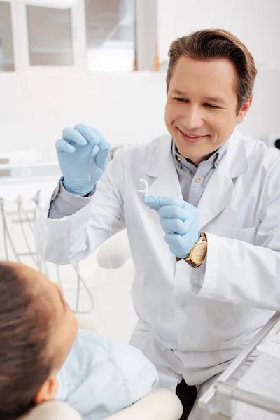 Избирательный фокус счастливого стоматолога, держащего зубную нить рядом с африканской американкой — стоковое фото