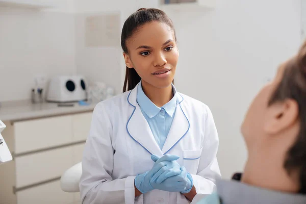 Selective focus of attractive african american dentist with clenched hands looking at patient — Stock Photo