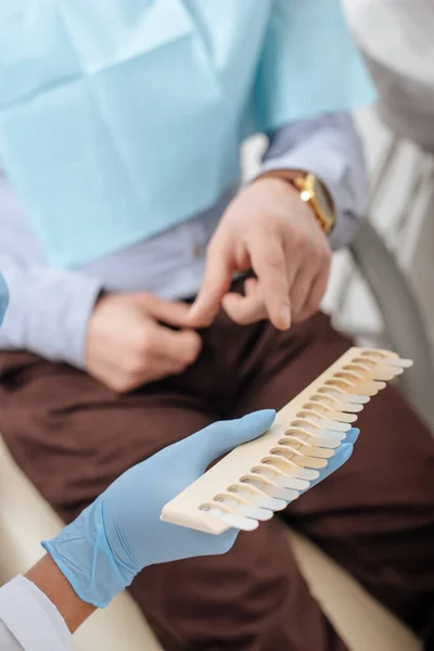 Vista recortada del hombre apuntando con el dedo a la paleta de dientes cerca del dentista en guantes de látex - foto de stock