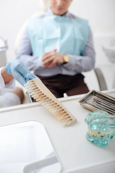 Foco seletivo do dentista na luva de látex tomando paleta de dentes perto do paciente — Fotografia de Stock