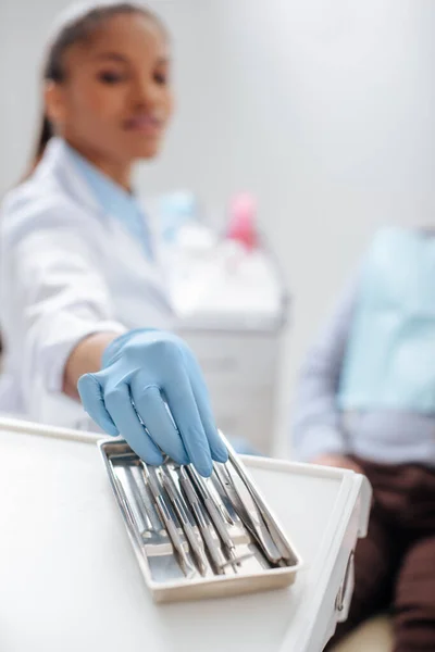 Foco seletivo do dentista afro-americano em luva de látex tomando instrumento dentário — Fotografia de Stock