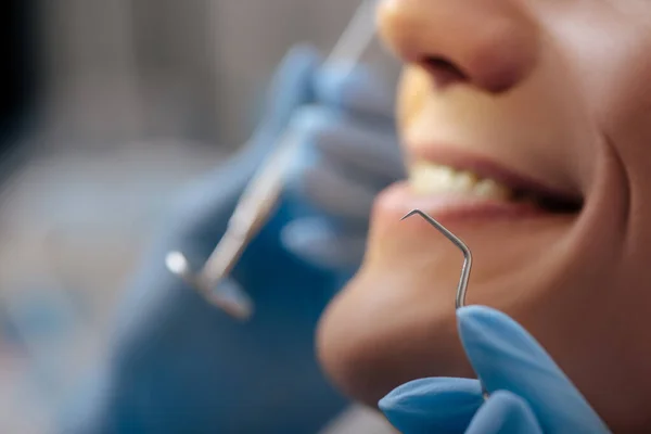 Vista recortada del dentista en guantes de látex sosteniendo instrumentos dentales cerca de hombre alegre - foto de stock