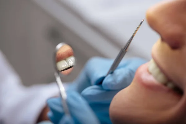 Vista recortada del dentista en guantes de látex sosteniendo instrumentos dentales cerca del hombre sonriente - foto de stock