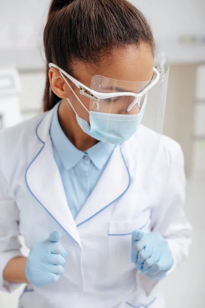Dentista afroamericano in maschera medica, scudo facciale e guanti in lattice — Foto stock