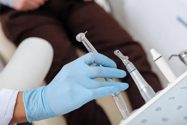 Vista recortada del dentista que toma el instrumento dental inoxidable cerca del paciente - foto de stock