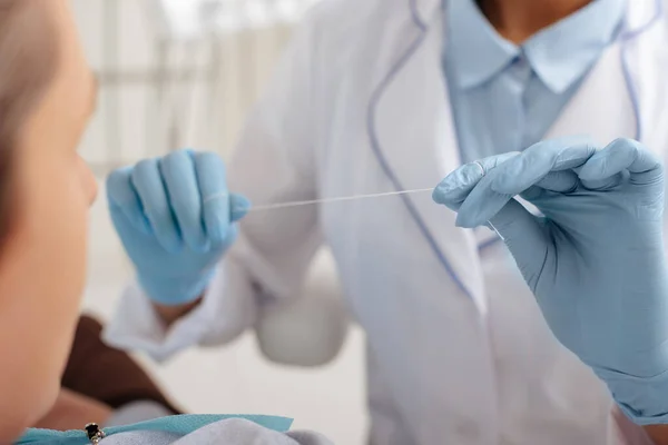 Enfoque selectivo del dentista en guantes de látex con hilo dental cerca del paciente - foto de stock