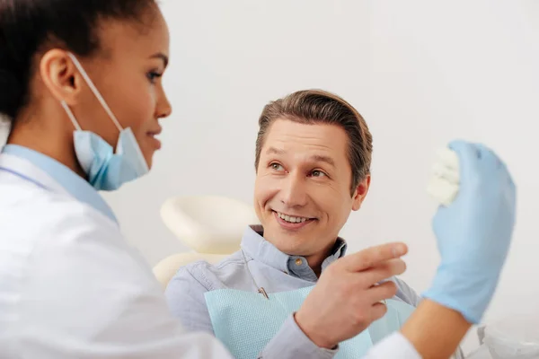 Selective focus of happy patient pointing with finger at teeth model near african american dentist in latex gloves — Stock Photo