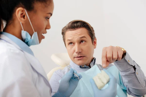 Foco seletivo do homem apontando com o dedo para o modelo de dentes perto de dentista afro-americano em luvas de látex — Fotografia de Stock
