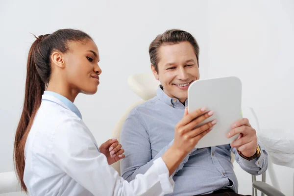Happy patient looking at mirror near cheerful african american dentist — Stock Photo