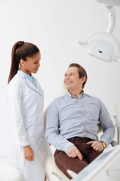 Patient heureux regardant souriant afro-américain dentiste en bretelles — Photo de stock