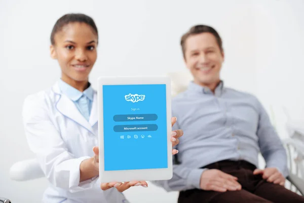 KYIV, UCRAINA - 12 MARZO 2020: focus selettivo di un allegro dentista afroamericano con tablet digitale con app skype sullo schermo vicino a un paziente felice — Foto stock