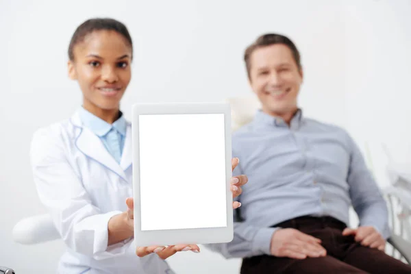 Selective focus of cheerful african american dentist holding digital tablet with white screen near happy patient — Stock Photo