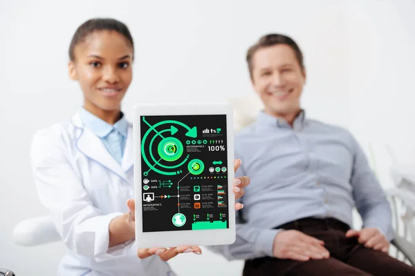 Selective focus of cheerful african american dentist holding digital tablet with charts and graphs on screen near happy patient — Stock Photo
