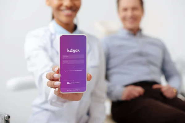 KYIV, UKRAINE - MARCH 12, 2020: selective focus of cheerful african american dentist holding smartphone with instagram app on screen near happy patient — Stock Photo