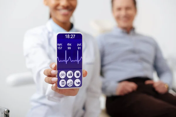 Selektiver Fokus des fröhlichen afrikanisch-amerikanischen Zahnarztes mit Smartphone mit medizinischer App auf dem Bildschirm in der Nähe eines glücklichen Patienten — Stockfoto