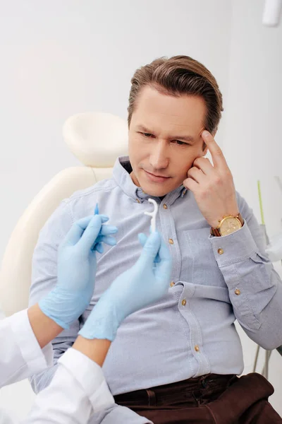 Dentist holding floss stick near pensive patient — Stock Photo