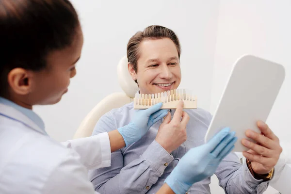 Selektiver Fokus eines afrikanisch-amerikanischen Zahnarztes mit Zähnen in der Nähe eines fröhlichen Patienten, der in den Spiegel schaut — Stockfoto