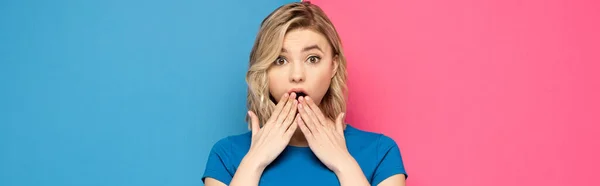 Shocked blonde girl looking at camera on pink and blue background, panoramic shot — Stock Photo