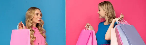 Panoramic shot of blonde women with shopping bags smiling at each other on pink and blue background — Stock Photo