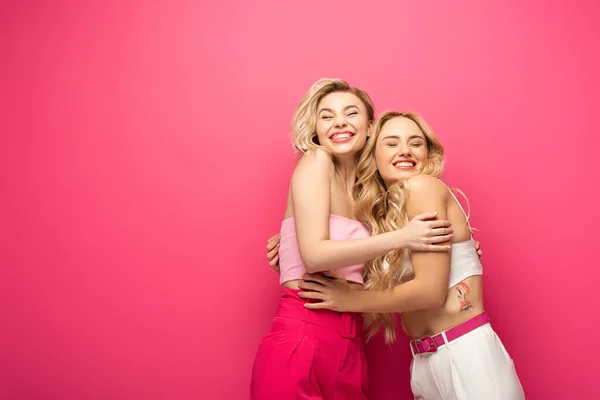 Smiling blonde friends embracing on pink background — Stock Photo