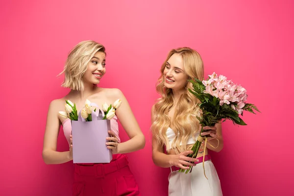 Blonde girls with bouquets smiling at each other on pink background — Stock Photo
