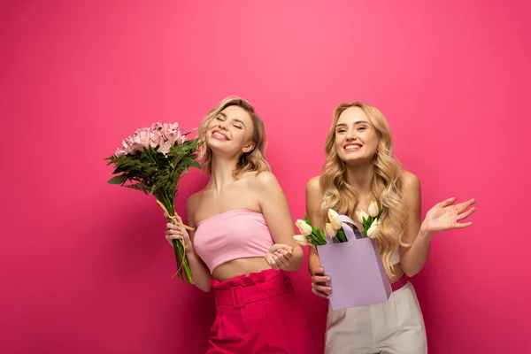 Chicas rubias positivas sosteniendo ramos florales sobre fondo rosa - foto de stock