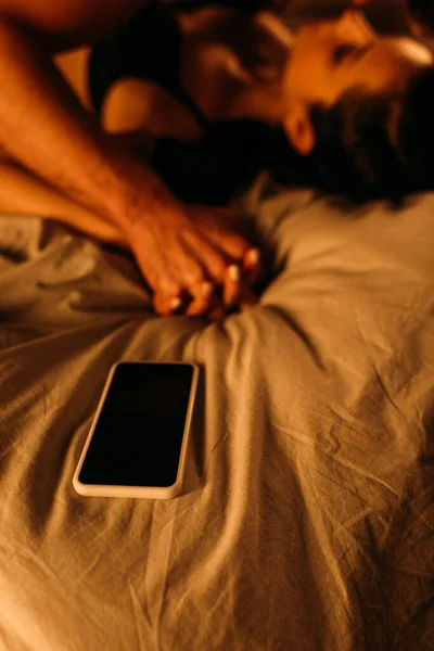 Foyer sélectif de couple avec les mains serrées couché près du smartphone sur le lit dans la chambre — Photo de stock