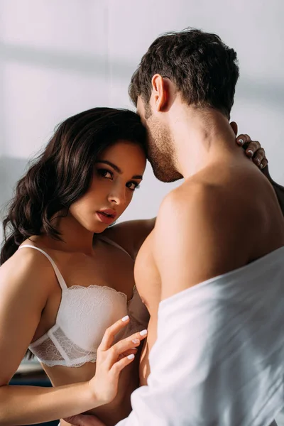 Sexy girl hugging businessman and looking at camera in bedroom — Stock Photo