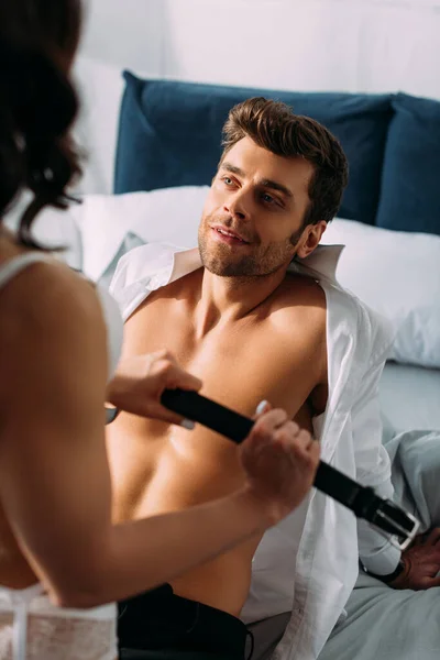 Selective focus of businessman looking at girl with male belt on bed in bedroom — Stock Photo