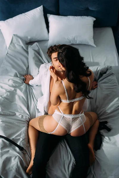 Vista de ángulo alto de chica caliente sentado en hombre de negocios con los ojos cerrados en la cama en el dormitorio - foto de stock