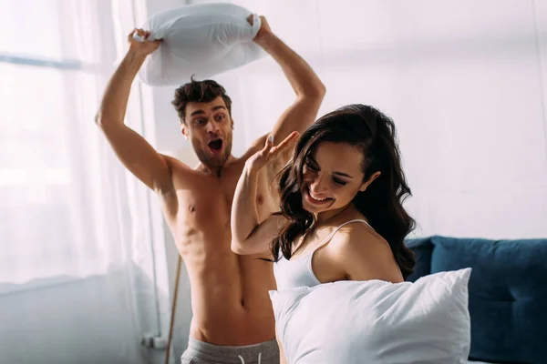 Menina sorrindo e mostrando sinal de parada para homem animado com travesseiro no quarto — Fotografia de Stock