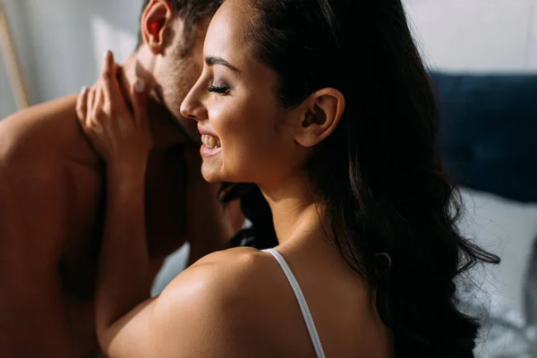 Novia con los ojos cerrados sonriendo y abrazando novio en el dormitorio - foto de stock